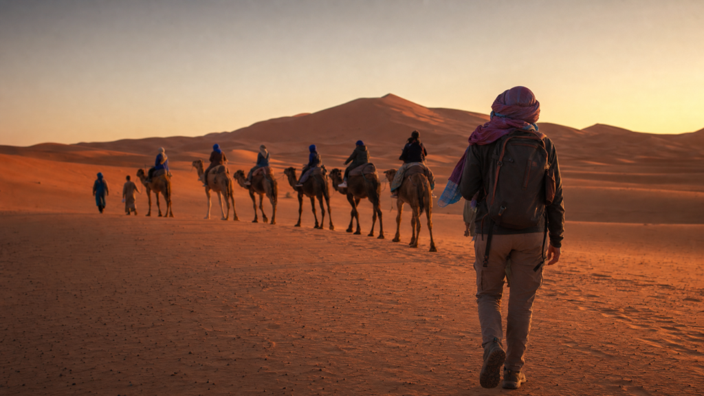 Traveler walking toward a camel caravan at sunset in the Merzouga Sahara Desert